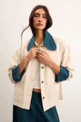 Sobrecamisa de algodón color beige, de corte holgado, con bolsillos frontales aplicados, cuello camisero y puños en contraste con estampado de cuadros en tonos verde oscuro. Cuenta con cierre frontal de botones metálicos.