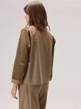 Camisa de manga larga con diseño bicolor en tonos tierra. Presenta un panel frontal y trasero en color beige, contrastado con mangas de un tono marrón más oscuro y textura satinada. Posee cuello redondo y corte recto.