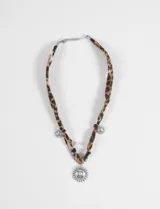 Collar con tira de tela estampada en animal print de leopardo, adornado con dijes metálicos plateados en forma de sol y una perla pequeña. Cuenta con un dije central grande de sol y cierre ajustable.