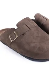 Zuecos cerrados al frente color negro, confeccionados en material símil gamuza. Presentan una tira ajustable con hebilla metálica en el empeine y una suela con detalle de corcho en el talón.