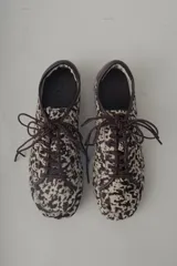 Zapatilla deportiva de mujer, modelo Champion Vane, con estampado animal print (vaca/manchas) en tonos marrón y beige. Presenta cordones marrones y detalles de cuero marrón liso en el talón. La suela es delgada y de color marrón claro.