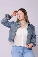 Campera de jean de mujer, color azul claro lavado, con corte cropped y estilo clásico. Presenta cuello camisero, botones metálicos frontales y bolsillos de parche en el pecho.