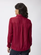 Blusa de satén color azul, con cuello camisero y cierre frontal parcial con cremallera. Presenta mangas largas con puños abotonados y un corte recto y fluido.