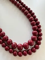 Collar de doble vuelta compuesto por cuentas esféricas de resina en color bordó con acabado brillante.