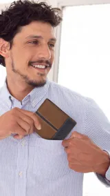 Billetera de cuero para hombre con diseño bicolor, combinando tonos marrón y negro. Cuenta con solapa central, múltiples ranuras para tarjetas, compartimento para billetes y visor transparente. Presenta el logo de la marca grabado en el frente.