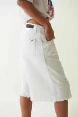 Bermuda de denim blanco de tiro bajo y corte holgado, con detalles desgastados y terminación desflecada en las perneras. Cuenta con trabillas en la cintura y cierre frontal con botón y cremallera.