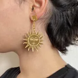 Par de aros colgantes plateados con forma de sol y rostro.