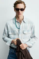 Camisa de algodón con efecto lavado, diseño a cuadros en tonos celestes y beige, cuello solapa, manga larga con puños abotonados y bolsillos frontales con solapa.