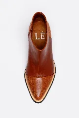 Botineta de cuero color suela, con diseño de punta fina y puntera texturizada con efecto reptil. Presenta una suela de madera clara con borde negro y cierre lateral interno.