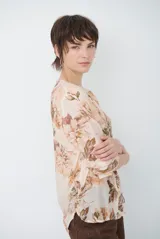 Camisa de manga larga con fondo verde y estampado floral en tonos rosados y beige, cuello redondo con pequeña abertura en V y cierre frontal con botones.
