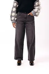 Jean de corte wide leg y tiro medio, confeccionado en denim de color gris oscuro con un lavado suave. Presenta una silueta recta y amplia, con cierre frontal y bolsillos laterales.