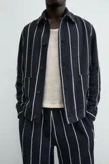 Sobrecamisa de hombre, corte relajado, color azul marino con rayas verticales blancas. Presenta cuello solapa, manga larga con puños abotonados, bolsillos de parche delanteros y cierre frontal de botones.