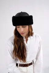 Gorro tipo cosaco reversible, confeccionado en cuero napalan negro con interior de piel sintética negra. Presenta una estructura de paneles en la parte superior y una banda ancha de pelo sintético que rodea la cabeza.