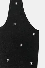 Top de punto negro con cuello halter y escote redondo, decorado con tachas metálicas plateadas distribuidas por toda la prenda.