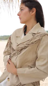 Chaqueta de gamuza color beige con diseño de flecos en el frente y las mangas. Presenta solapas clásicas, cierre frontal con botones y bolsillos laterales.