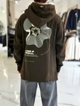 Canguro oversize chocolate con capucha, confeccionado con un diseño urbano que incluye un gran estampado gráfico en la espalda con líneas onduladas y texto.
