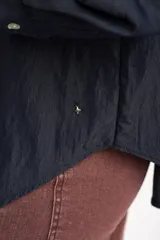 Camisa azul marino de corte oversize, con cuello clásico, cierre frontal con botones, mangas largas con puños anchos y un bolsillo aplicado en el pecho.