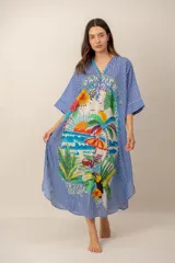 Vestido largo y holgado de fondo azul con rayas blancas, escote en V con botones frontales y mangas cortas amplias. Presenta un gran estampado central de temática tropical con palmeras, playa, tucán y vegetación.