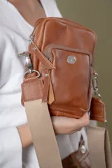 Bolso tipo bandolera de cuero vacuno color suela, con cierre frontal y compartimento principal. Incluye correa de cinta regulable y herrajes metálicos plateados.