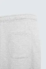 Pantalón jogger de corte relajado y pernera ancha, confeccionado en tejido de algodón con interior perchado. Cuenta con cintura elástica ajustable mediante cordón interior, bolsillos laterales y un bolsillo trasero de plastrón.