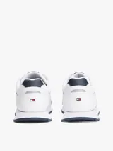Zapatillas deportivas Tommy Hilfiger de corte bajo, inspiradas en modelos clásicos de running. Presentan un exterior en mezcla de piel blanca con paneles de texturas mixtas, detalles de ventilación en la parte superior y suela de goma con tacos. Incluyen cordones y logo de la marca en el lateral, lengüeta y parte trasera.