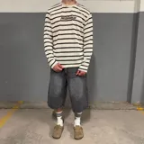 Sweater tejido a rayas horizontales grises y blancas con logo amarillo bordado en el pecho.