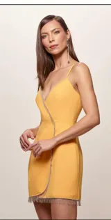 Vestido corto cruzado de color naranja con escote en V profundo, tirantes finos regulables y detalles de flecos plateados brillantes a lo largo del escote, los bordes y el dobladillo inferior. Presenta drapeado suave en la zona frontal de la falda.
