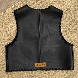 Chaleco de cuero negro con diseño artesanal, caracterizado por sus bordes rematados con tientos pasados a mano en todo su contorno.