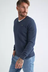 Sweater de tejido de punto color beige, con escote en V, mangas largas y puños y dobladillo acanalados. Presenta un pequeño logo bordado en el pecho.