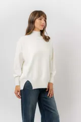 Sweater de tejido de punto color beige, con cuello alto, hombros caídos, mangas largas con puños acanalados y tajos laterales en el ruedo.