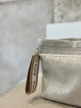 Sobre de mano color plateado con acabado texturizado y cierre superior. Incluye una correa de muñeca personalizada con la marca Rupia y detalles en yute.
