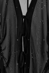 Camisa de cuello solapa con escote en pico y manga larga acabada en puño con abertura y lazo, confeccionada en tejido semitransparente de color negro con aplicación de tachas delanteras, cintura entallada con frunces laterales y cierre frontal con lazos.