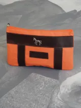 Sobre o cartuchera de lona fucsia con terminaciones y detalles de cuero marrón. Cuenta con cierre superior y aplique metálico de caballo en la parte frontal, además de una etiqueta de cuero con la marca grabada.