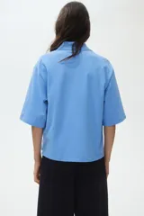 Remera polo de piqué de algodón en color celeste, con cuello acanalado, tapeta de tres botones, mangas al codo y hombros caídos. Presenta un corte holgado con bajo recto y aberturas laterales.