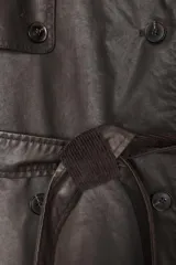 Gabardina larga de efecto encerado en color marrón oscuro, con cuello solapa y cierre frontal cruzado con botones. Presenta mangas largas con puños vueltos en pana, bolsillos laterales y cinturón ajustable de pana. Incluye pinza en la espalda.