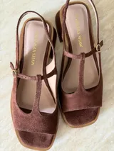 Sandalia de gamuza color marrón, con diseño tipo T-strap, taco cuadrado bajo y tira ajustable al talón con hebilla metálica dorada.