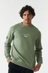 Buzo de felpa color verde oliva, con cuello redondo, puños y ruedo acanalados. Presenta un estampado frontal con texto en inglés y japonés junto al logo de la marca Mistral, y un detalle de etiqueta en la manga.