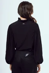Camisa blanca de manga larga abullonada, con cuello alto y volados delicados en el borde.