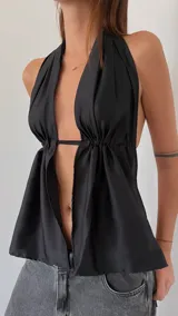 Top de satén negro con diseño halter, escote profundo y frunces laterales que crean un efecto drapeado. Presenta una abertura frontal con una tira fina de ajuste en la cintura.