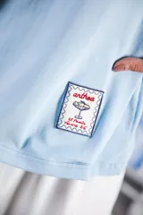 Remera de algodón color azul marino, corte relajado con hombro caído. Presenta cuello redondo blanco y bordado a mano en contraste en los puños de las mangas. Tiene un parche bordado en la parte inferior del frente.