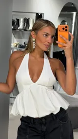 Top blanco con escote halter profundo y diseño peplum fluido, con corte ajustado en el busto y vuelo inferior.
