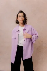 Camisa oversize de denim liviano color lila, con cuello camisero, mangas largas con puños, cierre frontal con botones y dos bolsillos delanteros con tapa. Presenta un diseño con hombros caídos y ruedo con terminación desflecada.