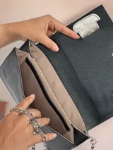 Sobre de cuero negro con aplique horizontal plateado y cadena metálica plateada.