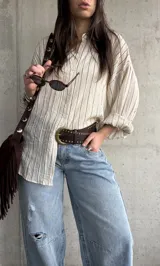 Camisa beige de rayas verticales, de calce relajado y tejido liviano, con mangas largas y cuello camisero.