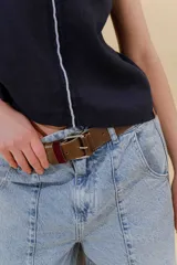 Pantalón de jean gris oscuro, estilo sastrero de tiro medio bajo y corte ancho (wide leg). Presenta costuras marcadas en el frente y un cinturón trenzado marrón con hebilla metálica.