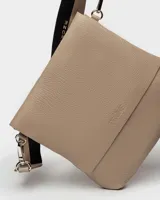 Bandolera color beige con correa ancha de tela negra con el nombre de la marca en blanco.