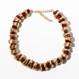 Collar corto con cuentas de piedra color borgoña y piezas de metal dorado con textura irregular.