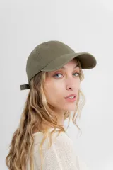 Gorra verde militar de diseño clásico con visera curva y aplique metálico plateado con la inscripción "Peach" en el lateral frontal. Cuenta con tira ajustable en la parte trasera.