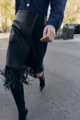Falda midi negra con efecto piel, diseño cruzado en el delantero y flecos en el bajo. Cierre lateral con cremallera oculta.