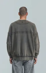 Buzo de cuello redondo, color gris oscuro con efecto desgastado (acid wash). Presenta costuras expuestas y detalles de roturas en los bordes. El calce es oversize y crop, con mangas largas abullonadas y puños y ruedo con terminación deshilachada y ondulada.